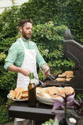 Mann bereitet Essen auf einem Grill zu, während er im Hof steht - CAVF46859