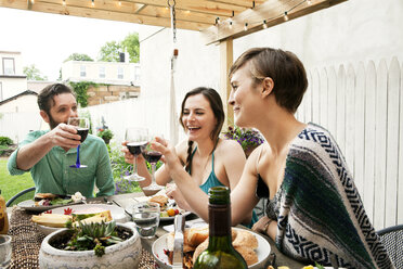 Friends toasting wineglasses while sitting at table in yard - CAVF46864