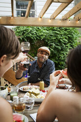 Man looking at female friends while sitting at table in yard - CAVF46865