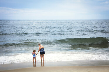 Rückansicht Enkelin und Großmutter halten sich an den Händen, während sie am Strand stehen - CAVF46877