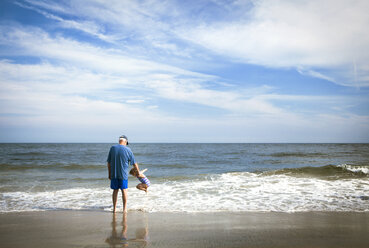 Großvater steht bei einem am Strand spielenden Mädchen - CAVF46886