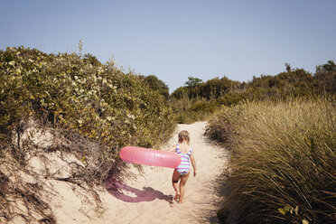 Rückansicht eines Mädchens, das einen aufblasbaren Ring trägt, während es auf Sand läuft - CAVF46900