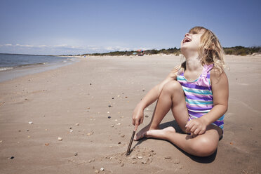Happy girl with head back sitting on sand at beach - CAVF46911