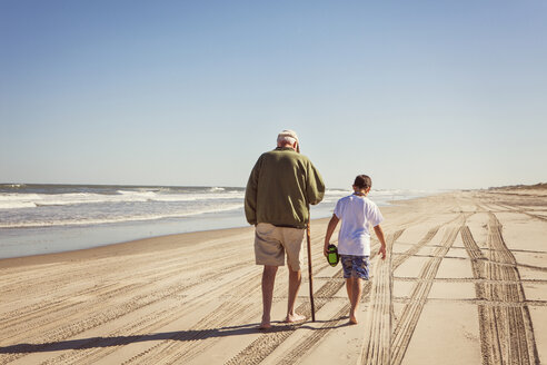 Rückansicht von Großvater und Enkel beim Spaziergang auf Sand gegen den klaren Himmel - CAVF46924