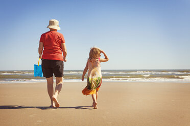 Rückansicht von Enkelin und Großmutter, die am Strand im Sand spazieren gehen - CAVF46925