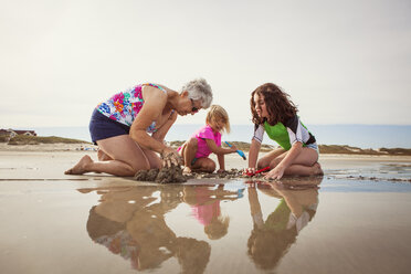 Granddaughters with grandmother digging while kneeling on sand at beach - CAVF46930