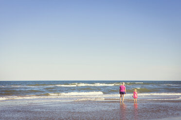 Rear view of grandmother and granddaughter standing in sea against clear sky - CAVF46936