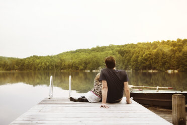 Rear view of girl with father sitting on pier - CAVF46963