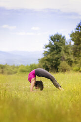 Seitenansicht einer Frau, die auf einer Wiese Yoga in Brückenstellung praktiziert - CAVF46989