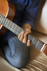 Ausgeschnittenes Bild einer Frau, die zu Hause auf dem Sofa sitzt und Gitarre übt - CAVF47009