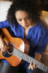 Hoher Blickwinkel einer Frau, die auf dem Sofa sitzend Gitarre übt - CAVF47010