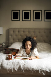 Frau liest ein Buch, während sie zu Hause auf dem Bett liegt - CAVF47015