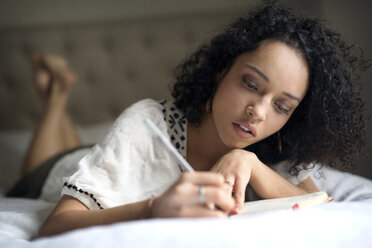 Woman writing while lying on bed - CAVF47018