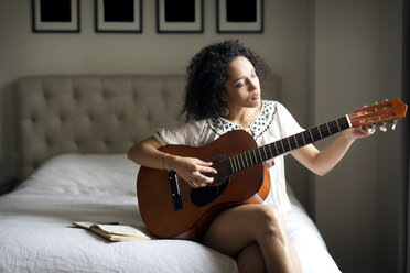 Woman adjusting guitar nodes while sitting on bed - CAVF47019
