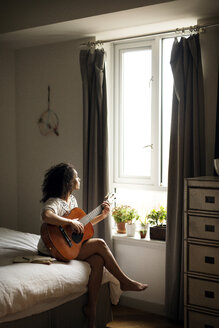 Frau schaut weg, während sie zu Hause Gitarre spielt - CAVF47020