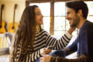 Happy couple talking while sitting on alcove window seat at home - CAVF47025