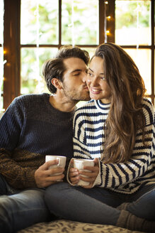 Mann küsst Freundin beim Kaffee auf Alkoven-Fensterplatz zu Hause - CAVF47033