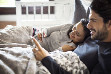 Ein Paar benutzt sein Smartphone, während es sich zu Hause im Bett ausruht - CAVF47050