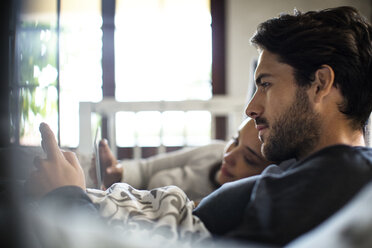 Nahaufnahme eines Paares, das zu Hause auf dem Bett liegend ein Smartphone benutzt - CAVF47052