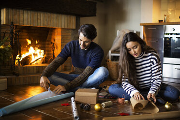 Couple wrapping gift boxes on floor by fireplace at home - CAVF47060