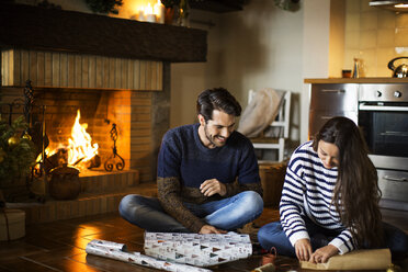 Happy couple wrapping gift boxes on floor by fireplace at home - CAVF47061