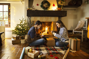Couple wrapping gift boxes on floor by fireplace at home - CAVF47062