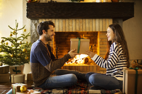 Glückliches Paar mit Weihnachtsgeschenk am Kamin zu Hause, lizenzfreies Stockfoto