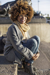 Portrait of happy woman sitting on steps in city - CAVF47080