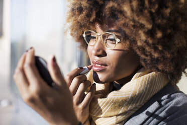 Close-up of woman applying lipstick at bus stop - CAVF47092