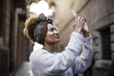 Woman photographing while standing by wall - CAVF47112