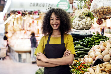 Porträt eines selbstbewussten Besitzers mit verschränkten Armen, der an einem Marktstand steht - CAVF47117