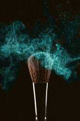 Close-up of make-up brush with turquoise face powder against black background - CAVF47157