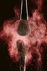 Close-up of make-up brushes with red face powder against black background - CAVF47159