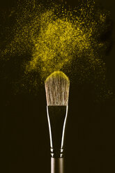 Close-up of make-up brush with yellow face powder against black background - CAVF47161