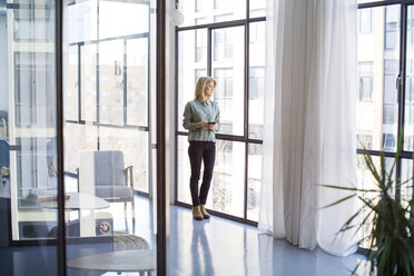 Businesswoman looking through window while standing in office - CAVF47162