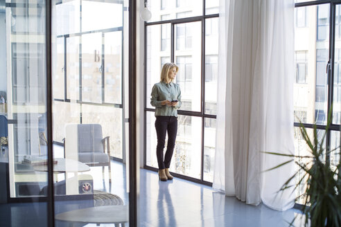 Geschäftsfrau schaut durch ein Fenster, während sie im Büro steht - CAVF47162