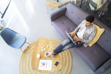 High angle view of businessman using laptop computer while sitting on sofa in office - CAVF47191