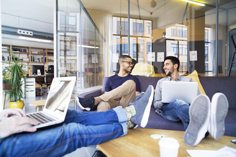 Niedriger Ausschnitt eines Geschäftsmannes, der einen Laptop benutzt, während seine Kollegen im Büro lächeln, lizenzfreies Stockfoto