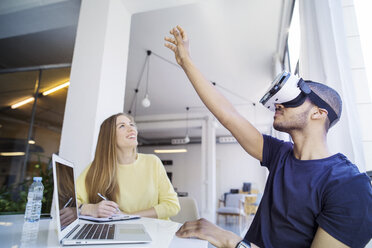 Colleagues examining virtual reality simulator in office - CAVF47198