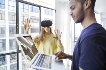 Businesswoman examining virtual reality simulator while male colleague using laptop - CAVF47200