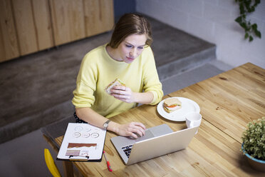 High angle view of businesswoman eating sandwich while using laptop at table - CAVF47205