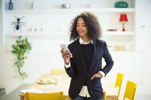 Lächelnde Geschäftsfrau, die ein Mobiltelefon benutzt, während sie am Tisch im Büro steht - CAVF47207
