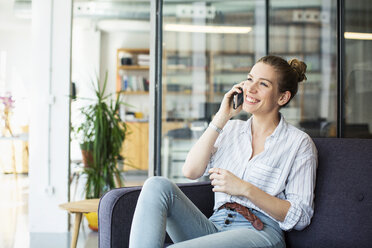 Glückliche Geschäftsfrau, die im Büro sitzend mit ihrem Handy telefoniert - CAVF47215