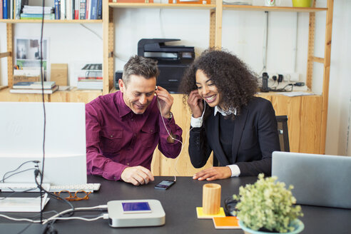 Glückliche Kollegen, die am Tisch im Büro ein Mobiltelefon benutzen - CAVF47226