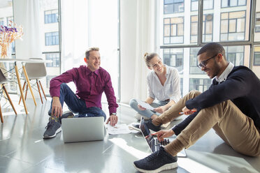 Business people discussing while sitting with laptop computers by window in office - CAVF47235