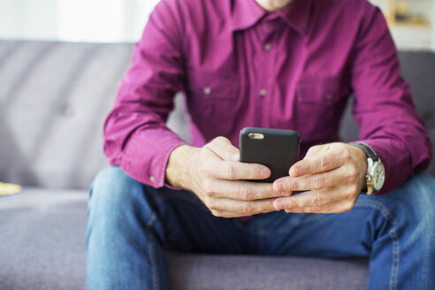 Mittelteil eines Geschäftsmannes, der auf dem Sofa im Büro ein Mobiltelefon benutzt - CAVF47242