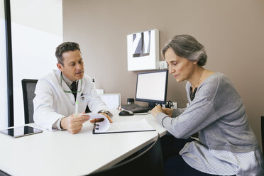 Arzt im Gespräch mit einem Patienten, während er im Krankenhaus an der Wand sitzt - CAVF47254