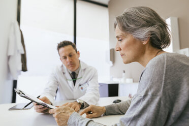 Nahaufnahme eines Arztes und eines Patienten, die auf ein Klemmbrett schauen, während sie in einer medizinischen Klinik sitzen - CAVF47255