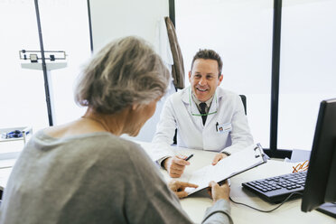 Glücklicher Arzt im Gespräch mit einem Patienten, während er im Krankenhaus an der Wand sitzt - CAVF47256