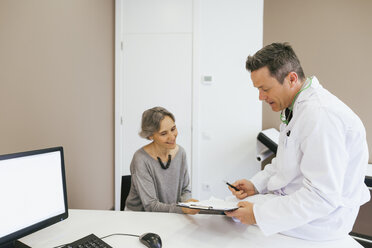 Glücklicher Arzt und Patient, der auf das Klemmbrett schaut, während er in einer medizinischen Klinik sitzt - CAVF47260